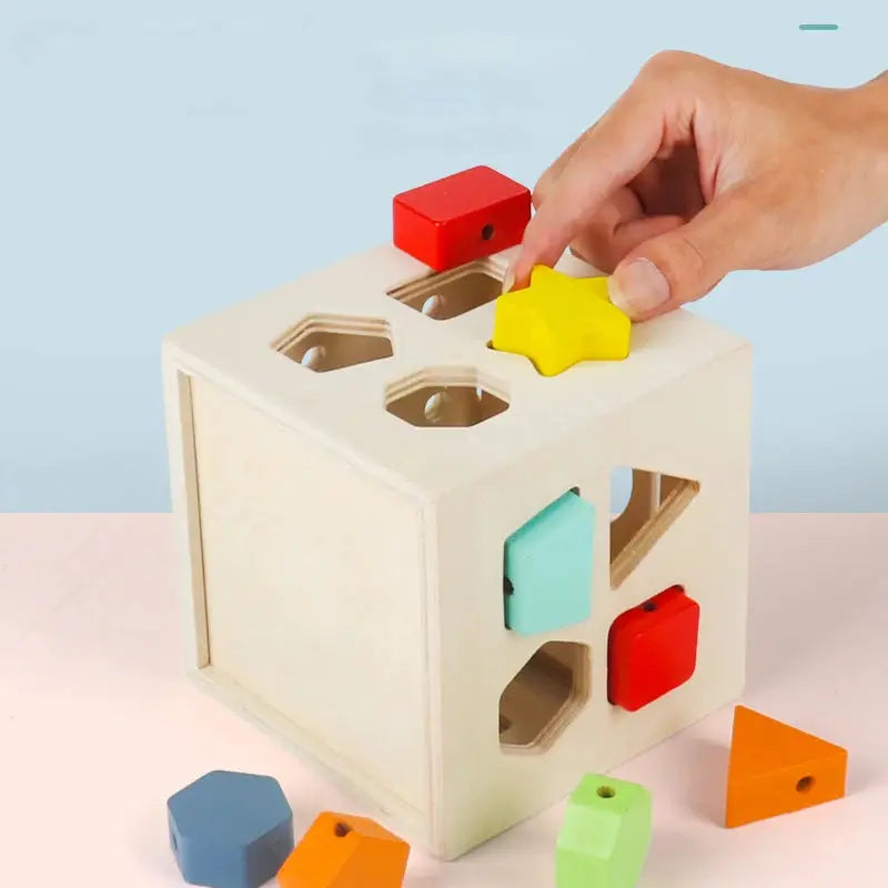 Hand placing star shape in wooden shape sorter cube.